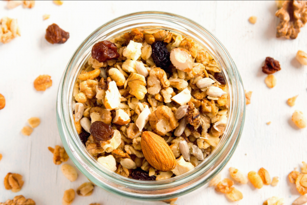 Nutty Granola Recipe Photo. Clear jar full of granola sitting on a white background. Bits of granola are on the table among the jar.