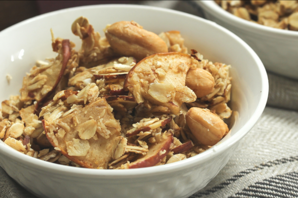 Nutty Granola Apple Bites Recipe Photo. Apples coated in granola in a white bowl. Background is white and grey.