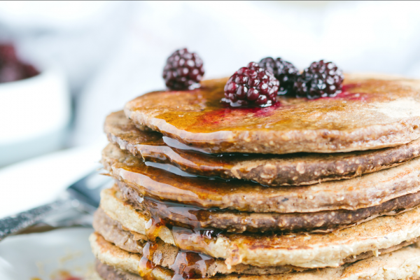 Orange Oatmeal Pancakes Recipe Photo. Stack of pancakes with berries and syrup on top, against a primarily white background.