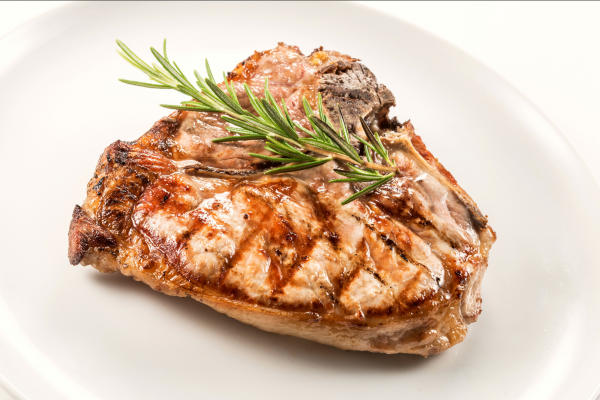 A single pork chop on a white plate, against a white background. Garnished with herbs.