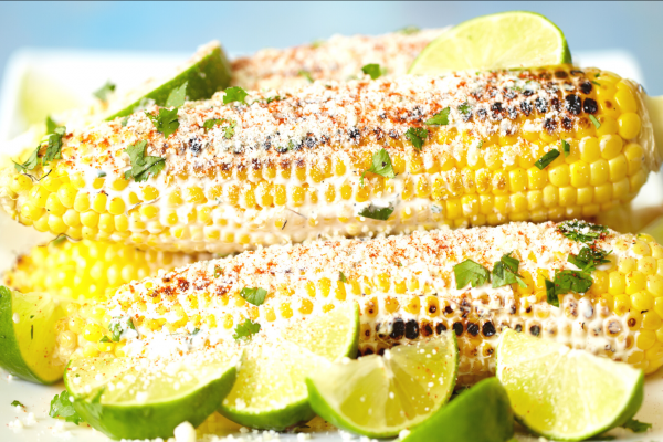 Prepared Corn on the Cob (Elote Preparado) Recipe Photo. Seasoned cooked cobs of corn on a white plate, with a blue background.