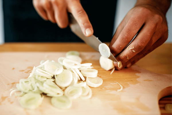 Hands cutting green onion on wooden chopping board