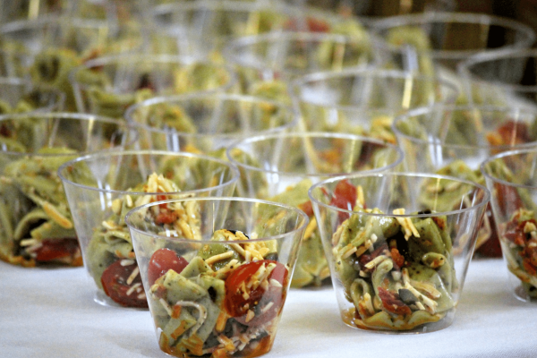 clear plastic cups with pasta salad made with cherry tomatoes