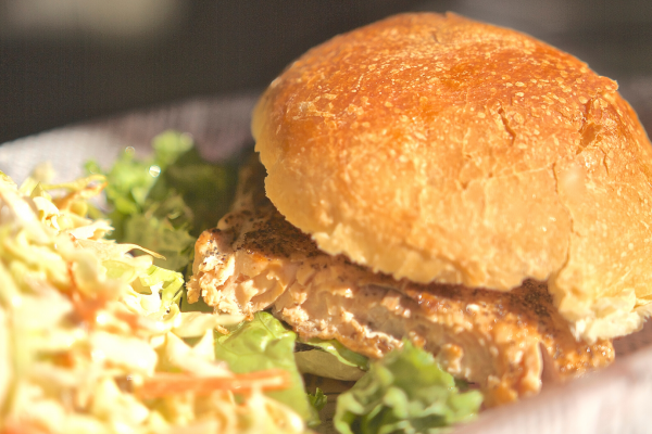 Photo of Salmon Burgers with Pickled Cucumbers. Burger is on a white plate, with coleslaw to the side.