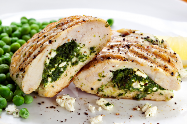 Spinach Stuffed Chicken Breasts with Tomato and Feta Recipe Photo. Grilled, stuffed chicken next to some peas, on a white plate.