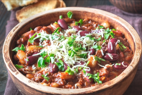Wooden bowl of turkey and bean chili, topped with herbs and cheese.