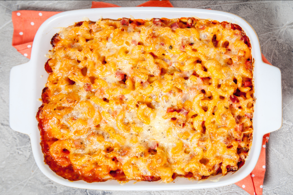 A white ceramic baking pan with freshly baked macaroni and cheese in it, against a grey background.